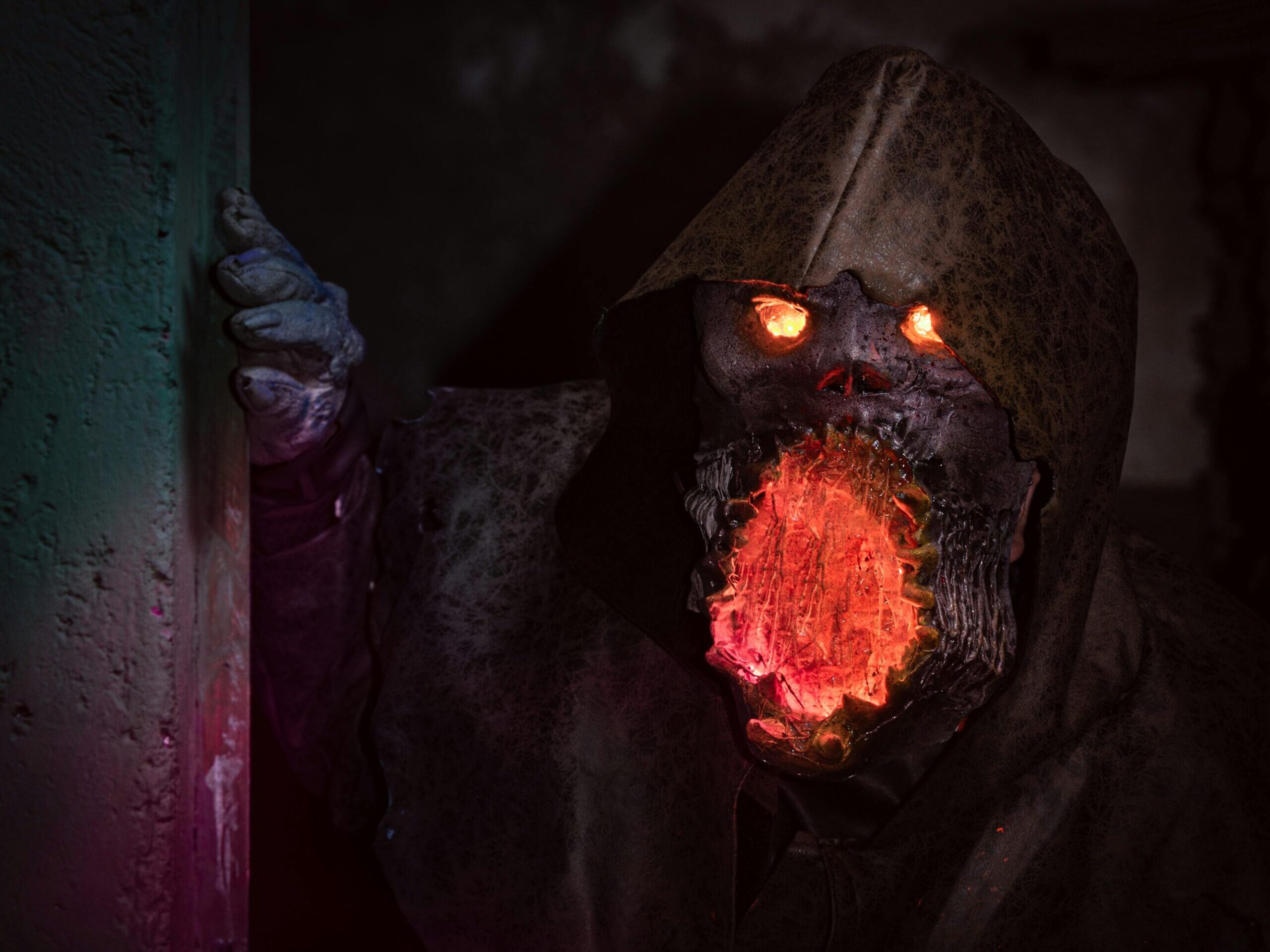 A menacing monster with glowing eyes and mouth in detailed horror cosplay peeking from a shadowy corner.